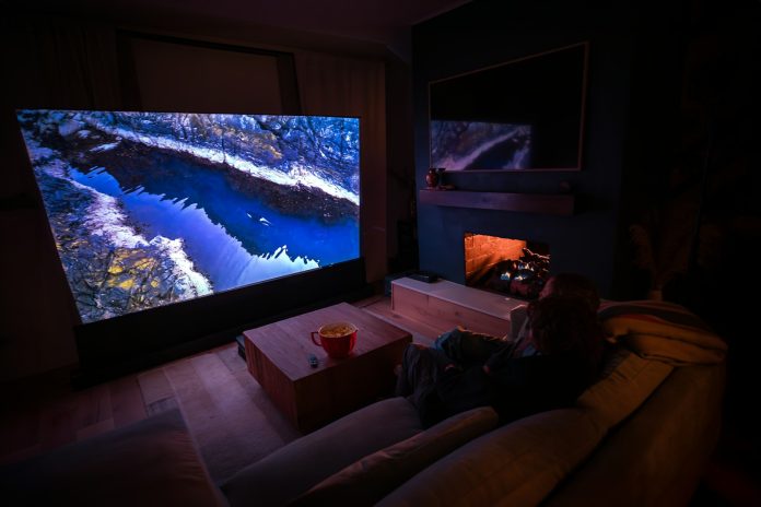Photo by AWOL Vision Projector A person sitting on a couch in front of a flat screen TV